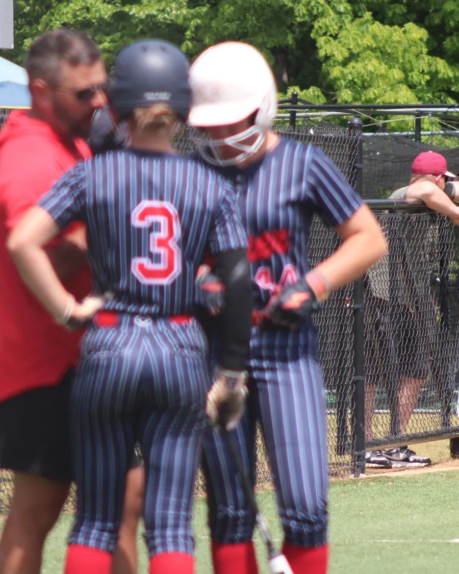 A coach talking with two players between innings at a travel softball tournament